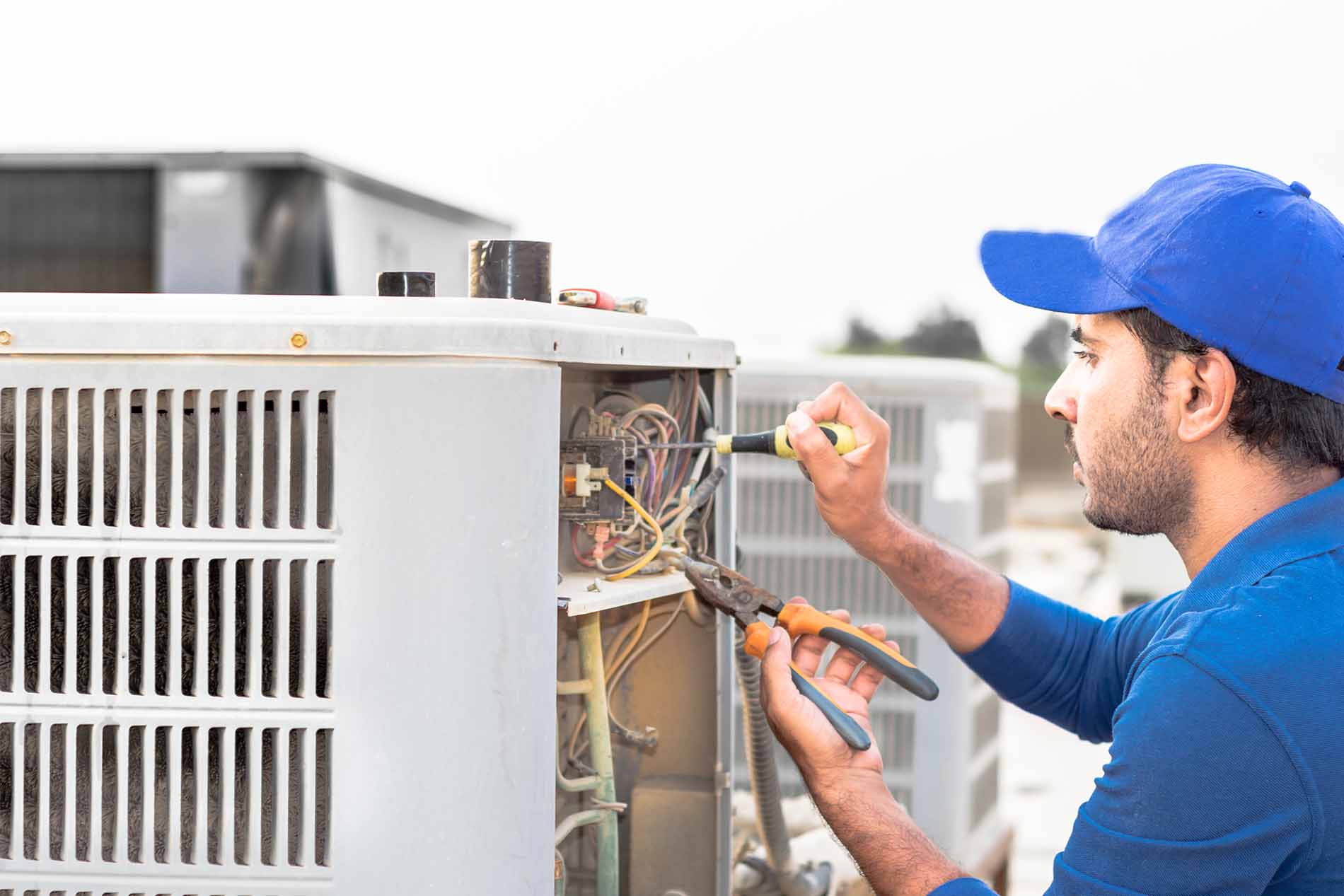 a professional electrician man is fixing a heavy air conditioner by his tools on the roof top and wearing blue color of uniform and head cap